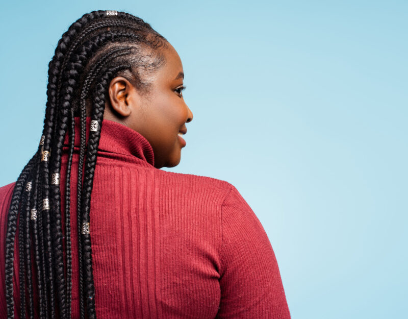 Back view portrait smiling African American woman with stylish braided hair looking away. Happy fashion model posing isolated on blue background, copy space. Customer, hair salon concept